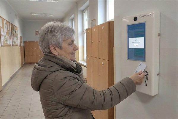 Krok 1 — babcia przykłada kartę zbliżeniową do czytnika terminala e-Świetlicy na szkolnym korytarzu